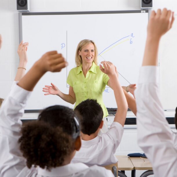 Rear view of class, students with their hands raised and Teacher stood at the front